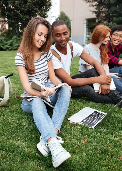 Happy people reading book and using laptop on lawn outdoors Happy people reading book and using laptop on lawn outdoors