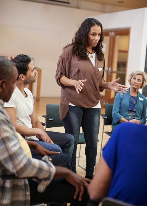 Woman Standing To Address Self Help Therapy Group Meeting In Community Center